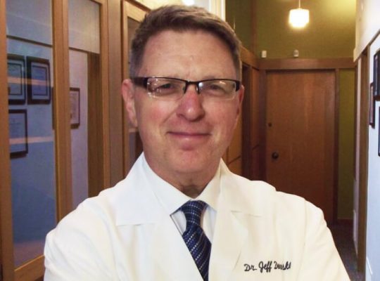 Dr. Jeff Doneskey in a dental coat, smiling confidently, in the Sleep Apnea and Facial Pain Center, emphasizing specialized care for sleep apnea and TMJ disorders.