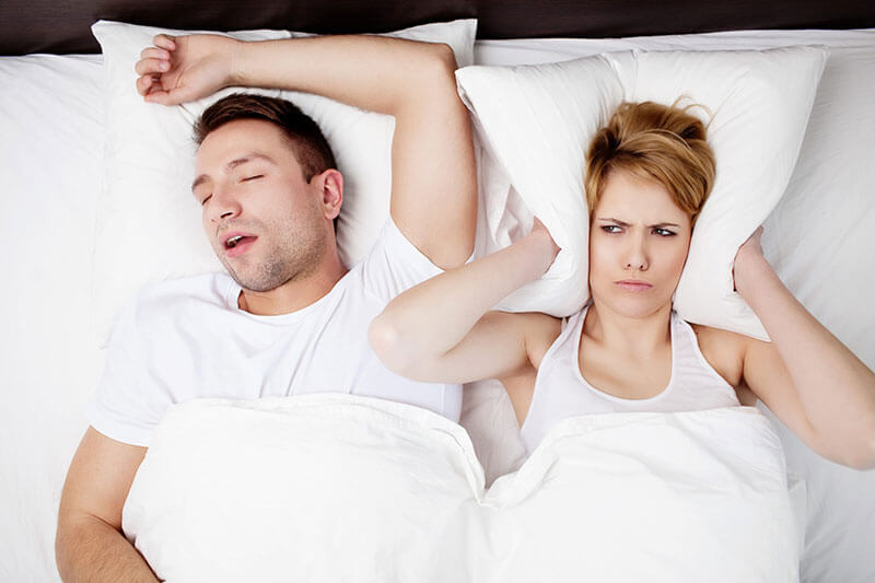 woman covering her ears with pillow because of snoring partner