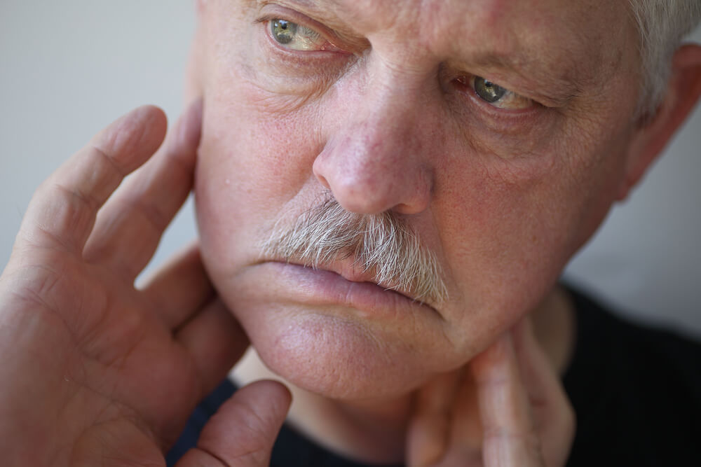 Elderly man experiencing facial pain, touching jaw area, related to TMJ disorders and facial pain conditions.