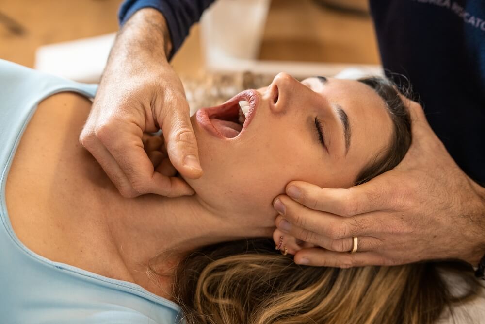 Patient receiving TMJ assessment, practitioner examining jaw and facial alignment, focus on facial pain diagnosis.
