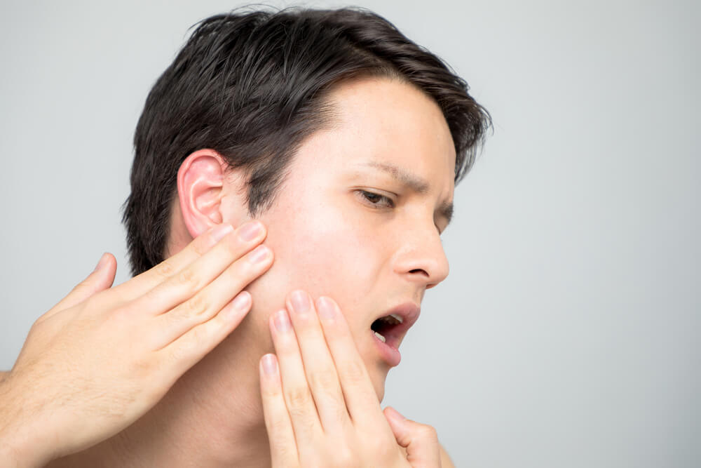 Man experiencing facial pain while touching his jaw, illustrating symptoms related to TMJ disorders, relevant to diagnosing facial pain conditions.